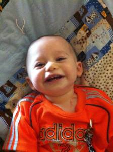 Sweet Xander smiling during his first few weeks of treatments, sitting on a prayer blanket made for him by a friend.